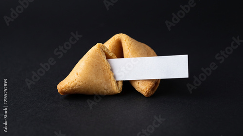 Fortune cookie with blank paper slip on black.