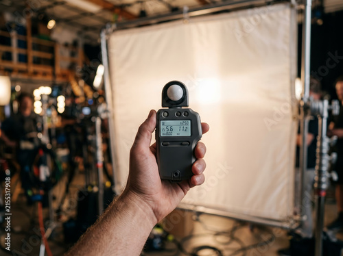 Filmmaker holding light meter to measure exposure on movie set stage