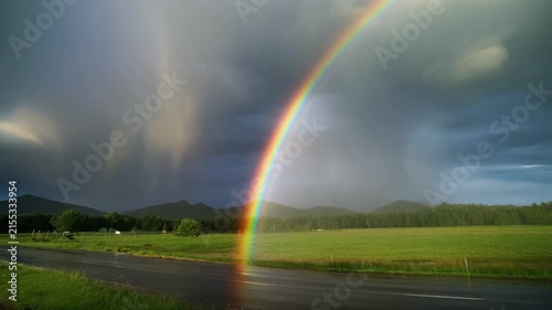 A vibrant rainbow arches over a green meadow against a backdrop of dark storm clouds.