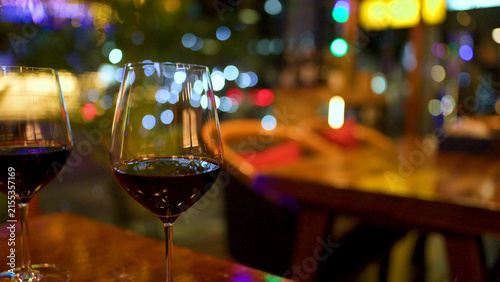Quadro su tela Two Red Wine Glasses on Wooden Table with Night City Bokeh