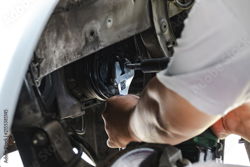 Close-up of a mechanic using an adjustable wrench and tool to repair or remove a car engine component in an auto workshop. Professional automotive maintenance and technical service concept.
