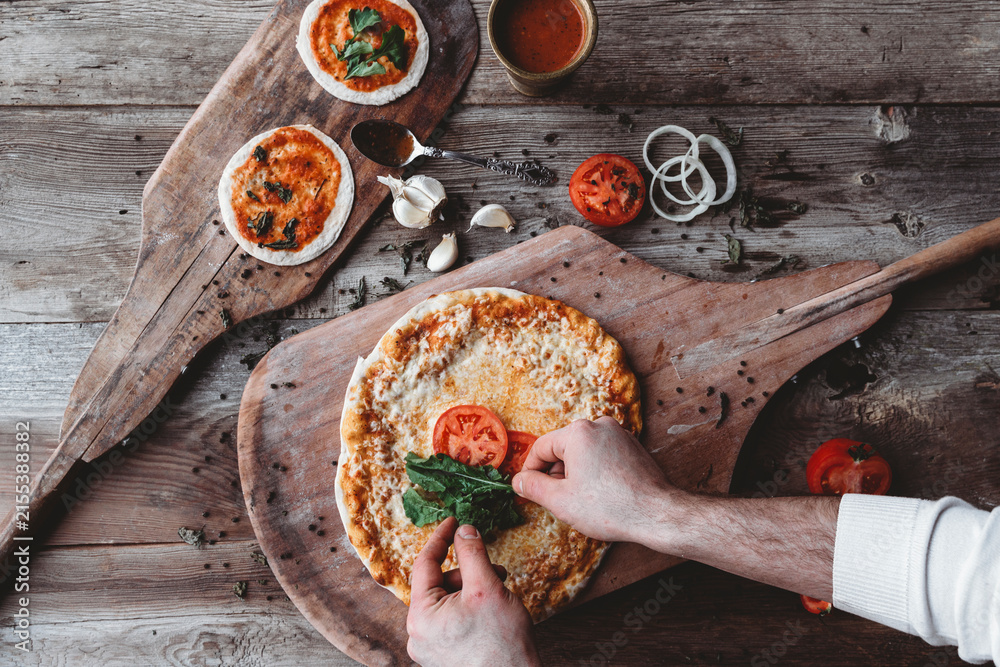 Naklejka premium Hands placing fresh toppings on a homemade pizza