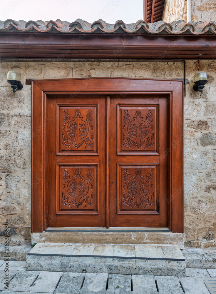 Fototapeta premium An ornate traditional wooden door with pomegranate carvings on an old stone house in the historic Kaleici district of Antalya, Turkey