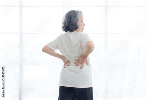 Asian elderly senior woman suffering severe back pain ache arm holding her shoulder on white background symbolizing chronic illness muscle strain repetitive strain injury arthritis aging healthcare.