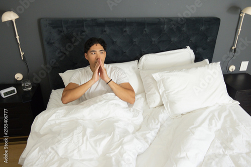 Obraz na płótnie Asian man sitting propped up in bed in master bedroom, white duvet, tufted headb