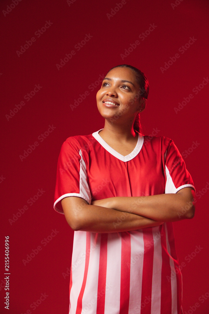 Fototapeta premium African American woman posing on red studio backdrop in red white striped jersey showing ear stud