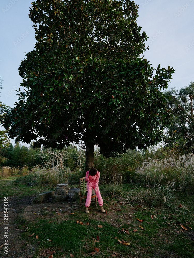 Obraz premium Child in pink clothing stands beneath a large tree in a park, autumn leaves scattered on the ground, conveying exploration and connection with nature.