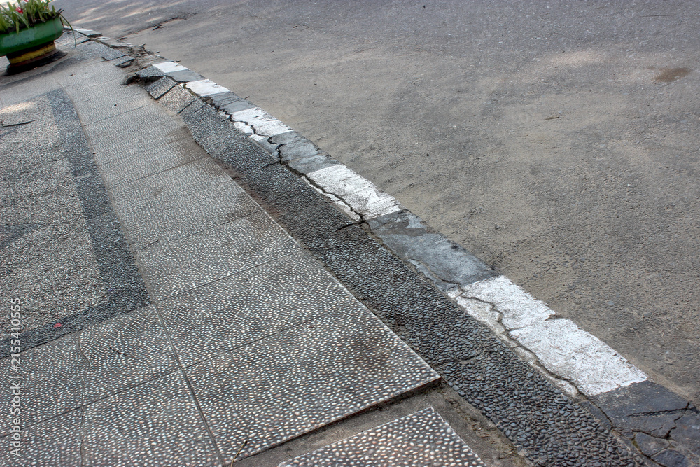 Obraz premium Along the edge of the concrete sidewalk, there are large and small cracks and uneven slabs lining the urban street.