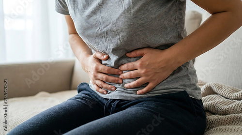Woman Holding Lower Abdomen with Both Hands While Sitting on Bed, Stomach Pain, Abdominal Cramps, Digestive Discomfort and Healthcare Concept