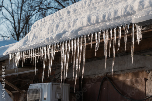 Long, sharp icicles hang from the snow-covered edge of the roof in the winter sun.