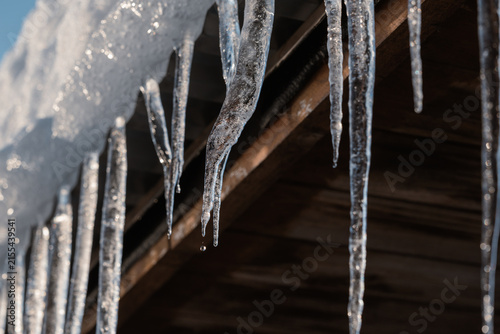 Long, sharp icicles hang from the snow-covered edge of the roof in the winter sun.