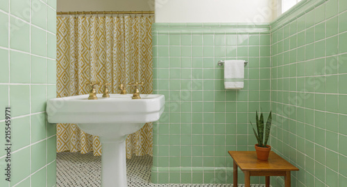 Vintage mid century washroom interior featuring mint green tiled walls and classic pedestal sink basin design with patterned yellow shower curtain showcases retro styled