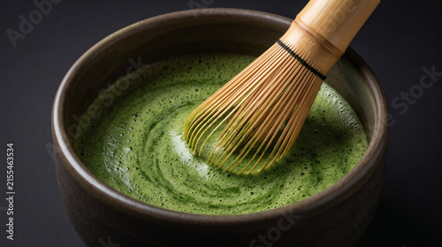 Close up of whisking green tea matcha with traditional bamboo chasen in dark ceramic bowl