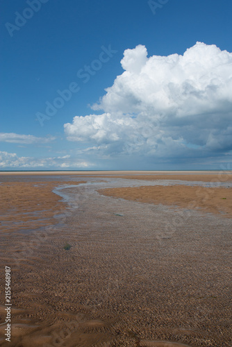The big, wide open space and big sky of the beaches in Norfolk, England, UK at low tide, with white clouds and blue sky.  The body of water in the foreground provides a leading line towards the sea.
