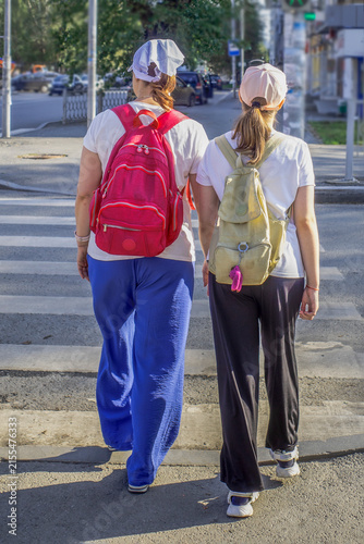 Mother and daughter with backpacks walking along a zebra crossing on a summer day