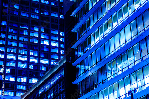 Modern glass skyscrapers at night in Tokyo financial district with glowing blue office windows and dynamic diagonal lines.