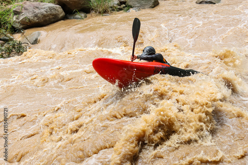 Konstfotografi Kayaker navigating muddy whitewater rapids in red kayak, wearing helmet and padd