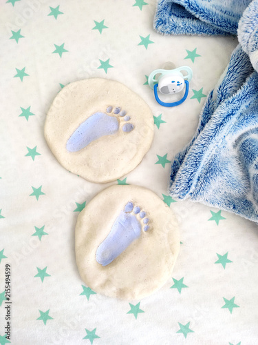 white sheet with green stars, the imprint of a child's foot on the salt dough, a blue baby pacifier, a boy child, birth, a mold of a small foot things accessories for the birth of a child, toys and 