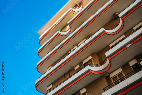 Canvas Print Low angle view of a modern Italian residential building facade with curved orange balconies against a clear blue sky in Italy