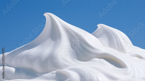 Creamy Peaks Against Blue Sky: Abstract composition of swirling white cream peaks resembling snowy mountains, set against a vibrant clear blue sky, suggesting freshness and indulgence.