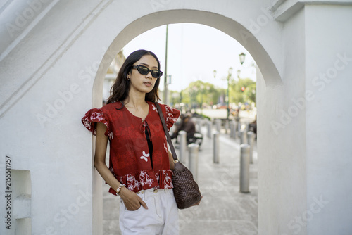 Stylish Asian woman in red batik blouse posing under an arch in Yogyakarta