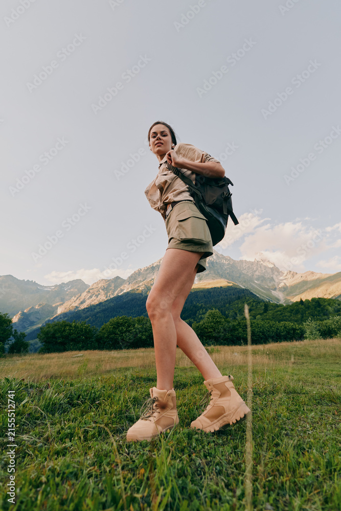 Obraz premium Active woman hiking through a field with a backpack, mountains in the distance, and clear sky. Outdoor lifestyle scene focused on exploration, nature, and travel moments.