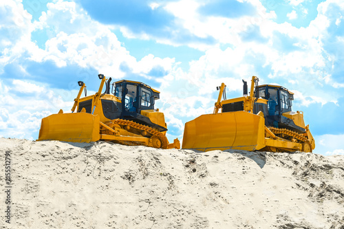 Modern bulldozer working on sand at a quarry or construction site. Heavy machinery moving and leveling sand during earthmoving and industrial operations.