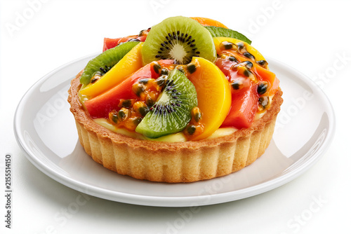 Tartelette aux fruits exotiques sur fond blanc, sur assiette blanche. Pâte brisée, crème pâtissière et fruits tropicaux (mangue, kiwi, passion, papaye) au nappage brillant
