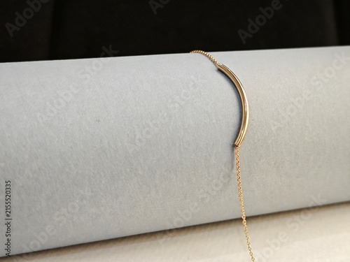Elegant minimalist gold necklace on a grey cylinder. Fine chain with a curved bar pendant