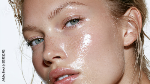 Young woman with natural freckles having radiant and dewy skin, showing a healthy glow, hydration, and a wet look, symbolizing fresh beauty and skincare