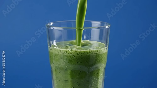 Healthy green smoothie pouring into a clear glass, vibrant beverage on a vivid blue background, nutrition and wellness, refreshing drink, slow motion video