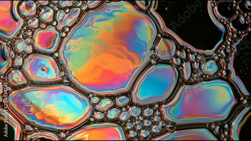 The camera captures the rippling movement of an oil film creating colorful reflections on a water surface in a public park.