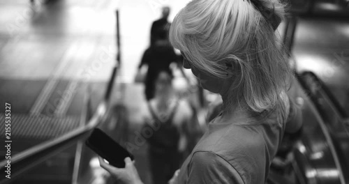 Caucasian senior woman using smartphone on airport escalator - Travel lifestyle and technology concept - UGC content - Black and white editing