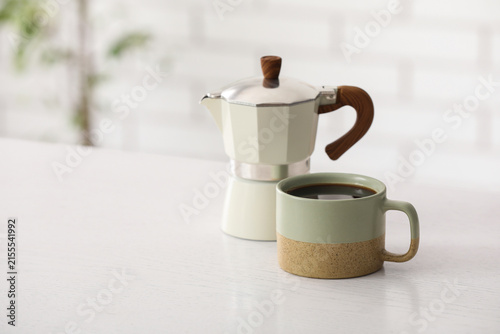 Foto Freshly brewed coffee in a two-tone ceramic mug next to a modern moka pot on a w