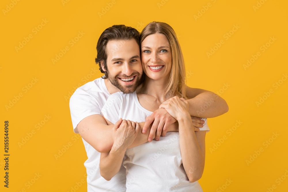 Fototapeta premium Happy Caucasian Couple Smiling And Embracing Each Other With Joyful Expressions, Showing Love And Affection, Standing Together In Studio Against Vibrant Yellow Background, Family Concept.