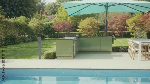 Luxury outdoor kitchen setup beside a swimming pool and manicured lawn
