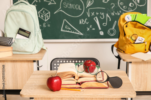 School desk with books, apples, eyeglasses and magnifying glass in classroom,...