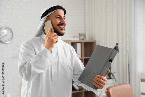 Arab businessman with folder talking by mobile phone in office