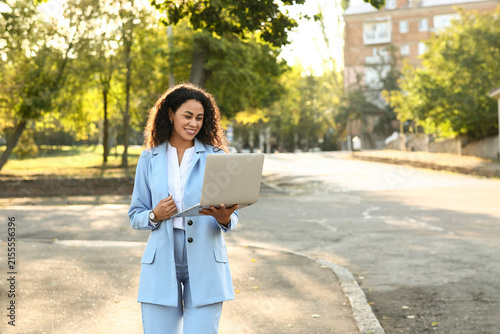 Beautiful young happy African-American businesswoman with laptop in park