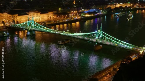 A stunning night view of the green Liberty Bridge illuminated over the Danube River in Budapest featuring glowing city lights and reflections on the water surface