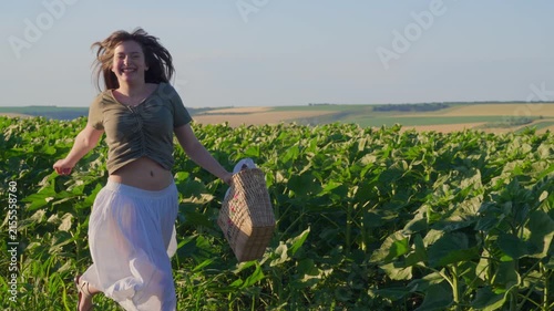 A joyful young female teenager running through a rural agricultural field carrying a wicker basket in the sunlight