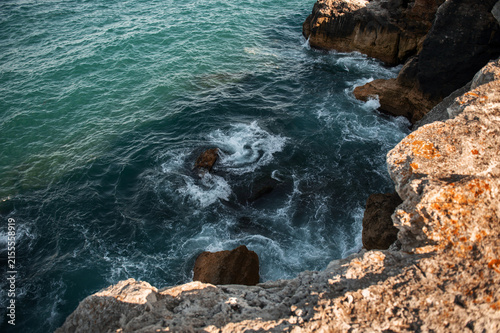 Aerial view of ocean waves crashing against rocky cliffs and large stones