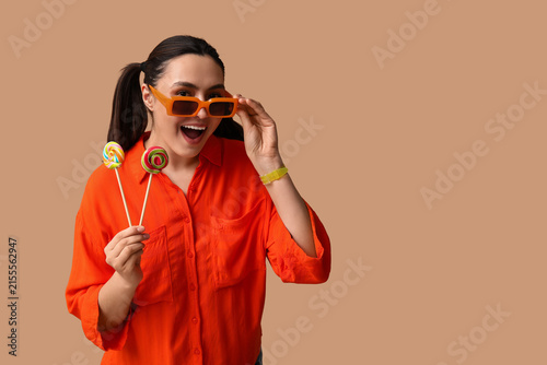 Beautiful young woman in sunglasses with sweet lollipops on brown background
