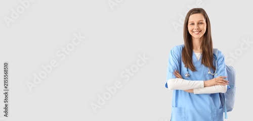 Smiling young female medical student in blue scrubs with stethoscope and back...