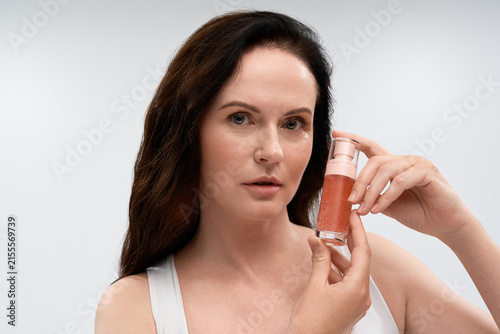 Принти на полотні Elegant mature woman showcasing skincare product in serene studio ambiance