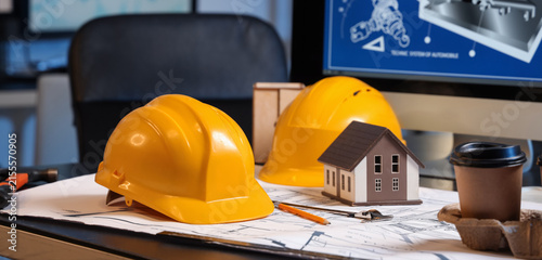 Construction site planning with yellow hard hats house model and blueprints o...