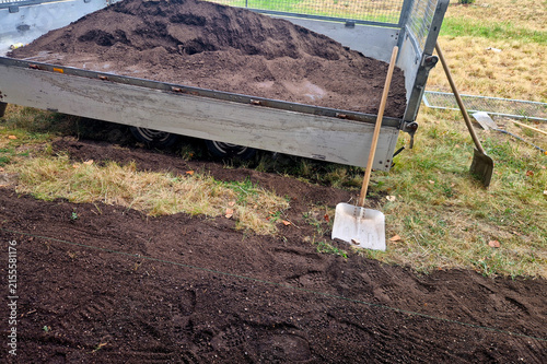 фотографія a trailer full of dark soil or compost and a garden shovel stuck in the grass next to it