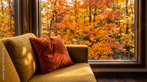 Autumn interior close-up, yellow sofa against living painting window of fall foliage, warm seasonal colors throughout, shallow depth of field