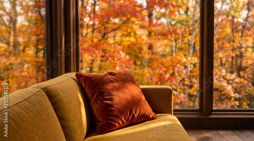 Mustard sofa corner with rust velvet cushion, large window framing orange-red autumn canopy, amber leaf light patches on sofa, autumn warmth