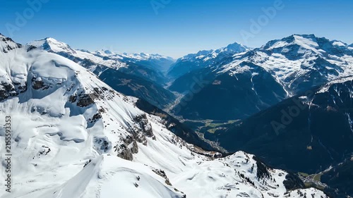 Breathtaking panoramic view of snow-covered mountains and a deep valley with evergreen trees under a clear blue sky